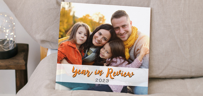 Square closed photobook on bed showing a family outside during autumn that reads 'year in review 2023.