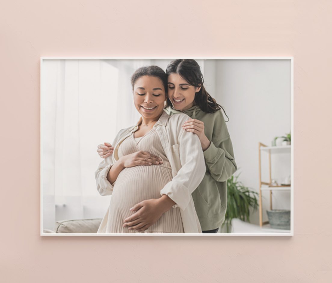 A woman holding her baby bump with her partner holding her from behind