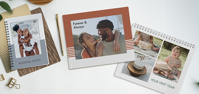 A notebook showing photo of couple that reads 'wedding planning', a photobook that shows a young couple that reads 'forever & always and a closed calendar showing photos of a Childs first birthday that reads 'your first year'.
